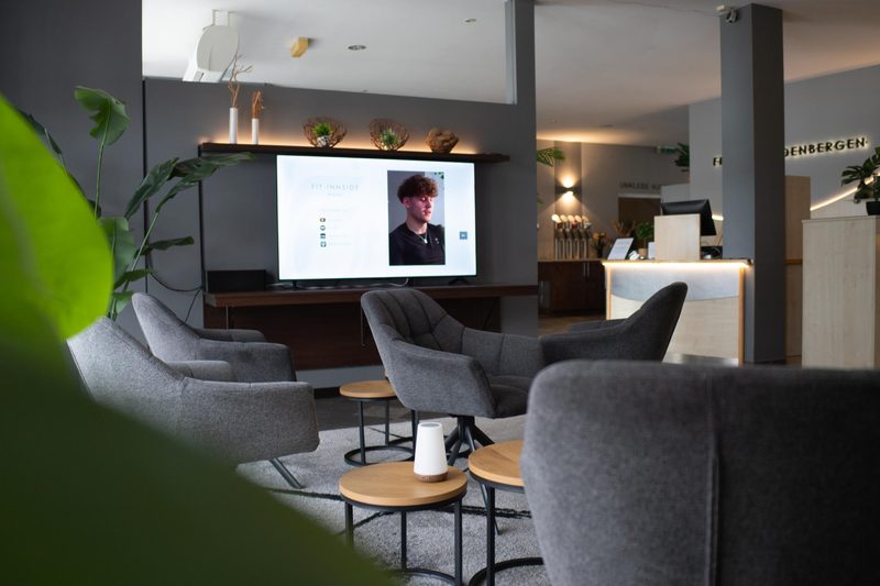 Loungebereich mit Sesseln und Bildschirm mit FIT-INNSIDE Podcast im Fit-Inn Heldenbergen